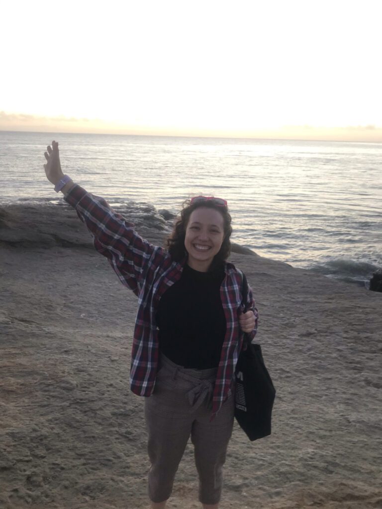 I am standing in front of the Pacific Ocean. I am smiling and my hair is pulled back by a pair of sunglasses. My hair is also brown.