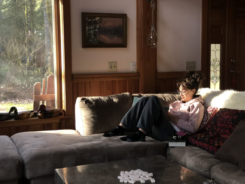 I am sitting on a couch in Rhodendron Oregon. I have my brown hair tied back in a bun and I have bangs.