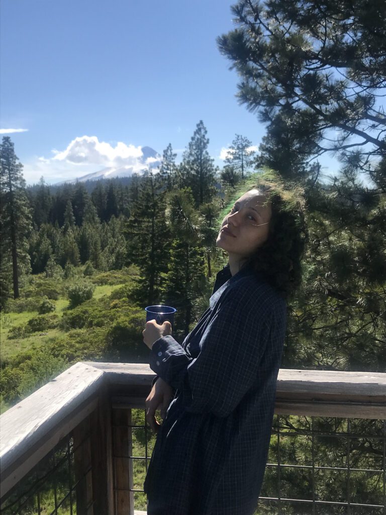 I am standing on a fire lookout tower in front of Mt. Hood. My hair is down and dyed dark green.