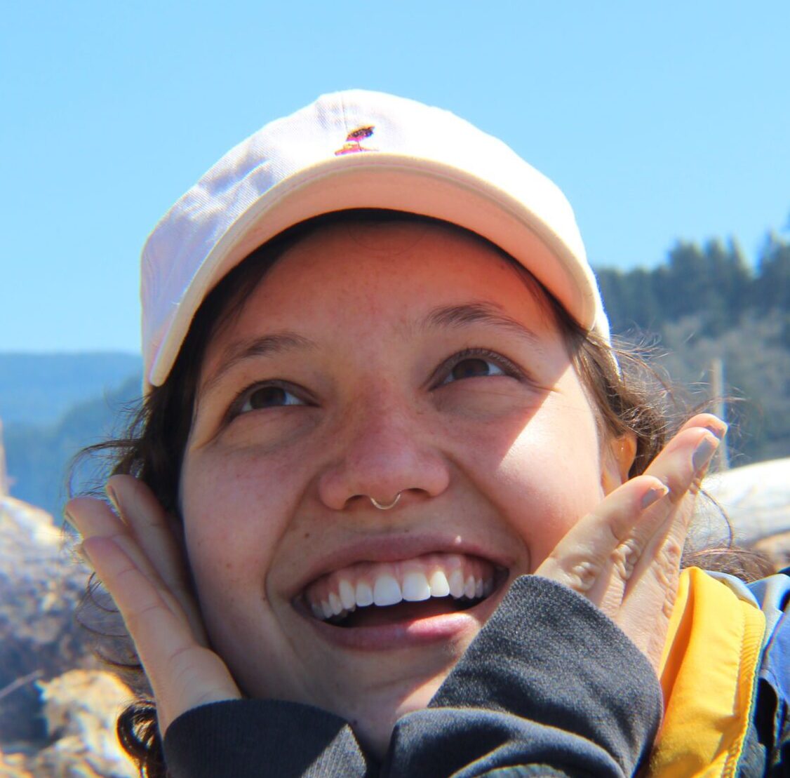 I am smiling and looking up. My hair is brown, up, and back. I am wearing a hat.